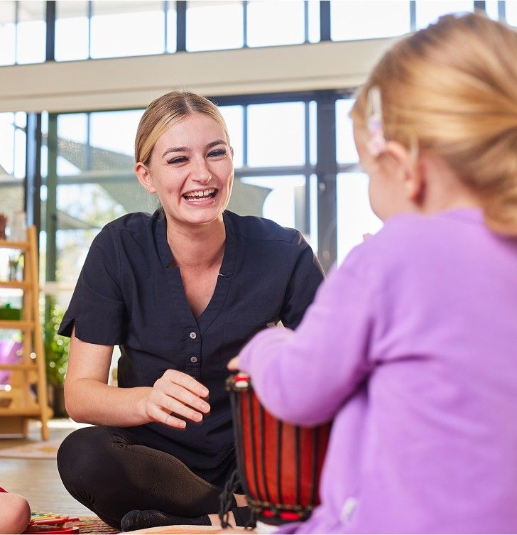 A smiling female educator helps a young girl in gloves with a gardening activity